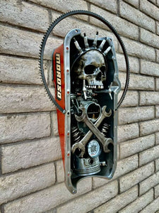 "Dead Pan" reclaimed metal wall sculpture by Paul Klaine, 25-inch artwork featuring skull, crossed wrenches, spark plugs, gears, and oil pressure gauge in steel frame.