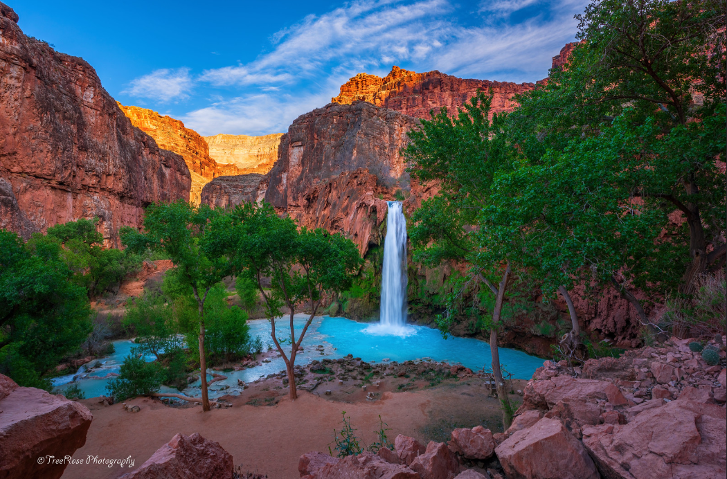 Havasu Falls in Havasupai, Arizona with turquoise blue water, red rock canyon walls, and lush green trees under a bright blue sky, Southwest waterfall landscape photograph.