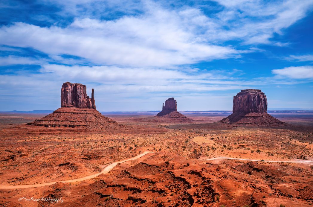 Monument Valley panoramic view of the Mittens and Merrick Butte under a bright blue sky, iconic red rock desert landscape on the Arizona–Utah border.