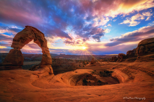 Delicate Arch in Arches National Park, Moab, Utah at sunset with snow-capped La Sal Mountains in the background, dramatic red rock desert landscape photograph.