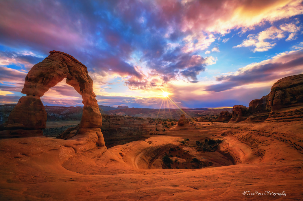 Delicate Arch in Arches National Park, Moab, Utah at sunset with snow-capped La Sal Mountains in the background, dramatic red rock desert landscape photograph.