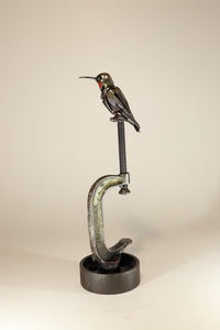 "Ruby" reclaimed metal sculpture by David Groenjes, 12-inch tall hummingbird with ruby-red throat perched on a steel clamp, crafted from salvaged industrial materials.